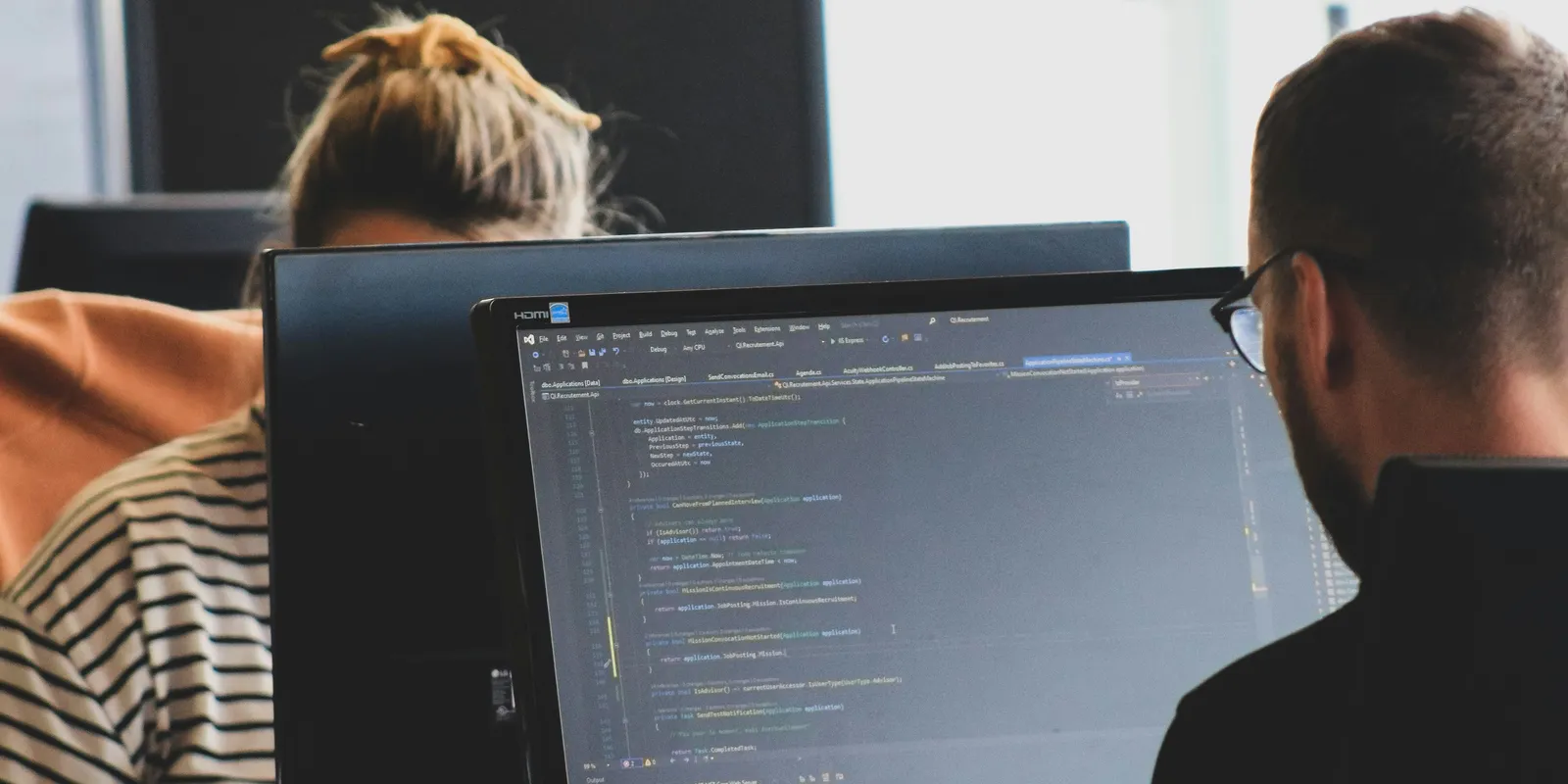 Two developers working side by side at monitors showing code